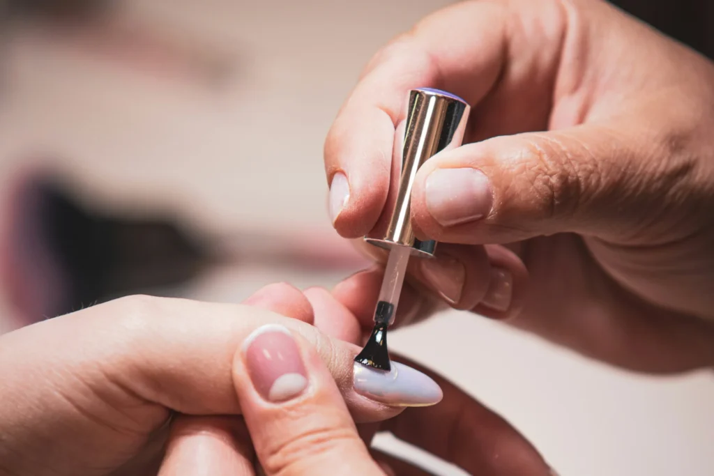Zbliżenie na dłoń, która precyzyjnie nakłada lakier na paznokieć, tworząc estetyczny manicure.