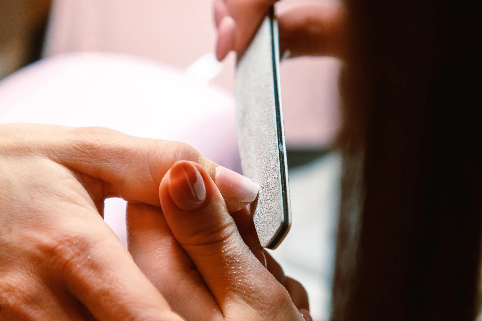 Zbliżenie na dłoń podczas profesjonalnego manicure, kosmetyczka używa pilnika do paznokci.
